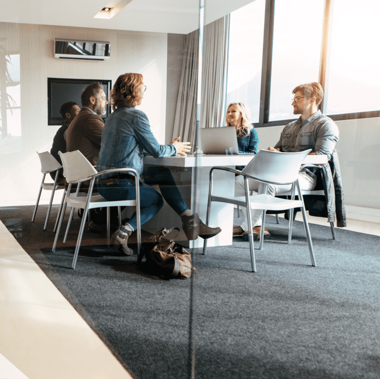 Group of business people sitting around a conference table in a brightly lit board room.